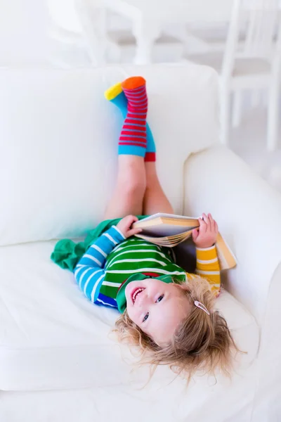 Petite fille lisant un livre sur un canapé blanc — Photo