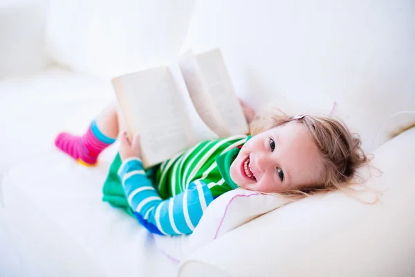 Little girl reading a book on a white couch