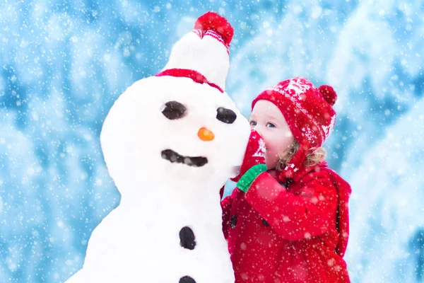 Kleines Mädchen spielt mit einem Schneemann — Stockfoto