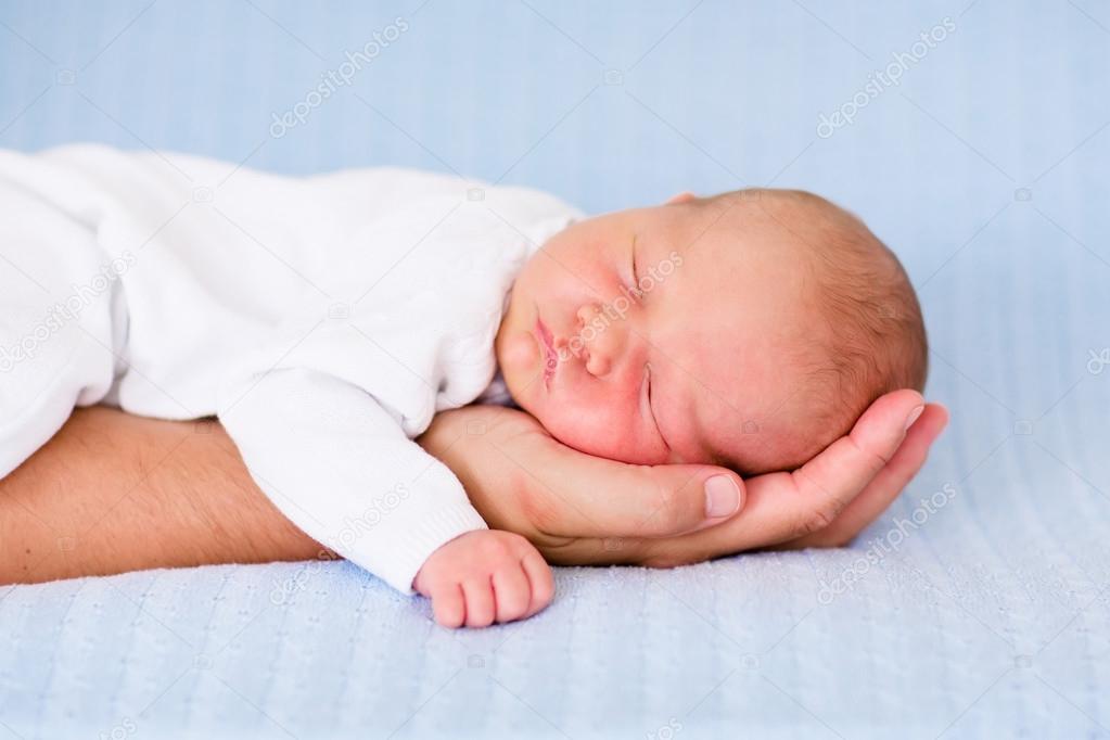 Newborn baby boy sleeping on the hand of his father