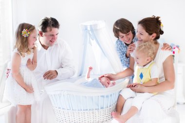 Family playing with newborn child in white bassinet