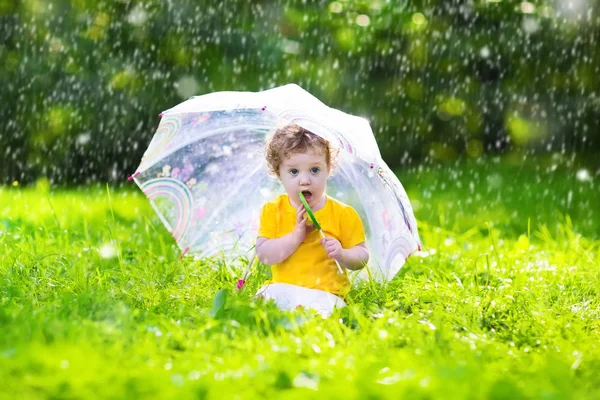 Little girl with colorful umbrella playing in the rain — Stok fotoğraf