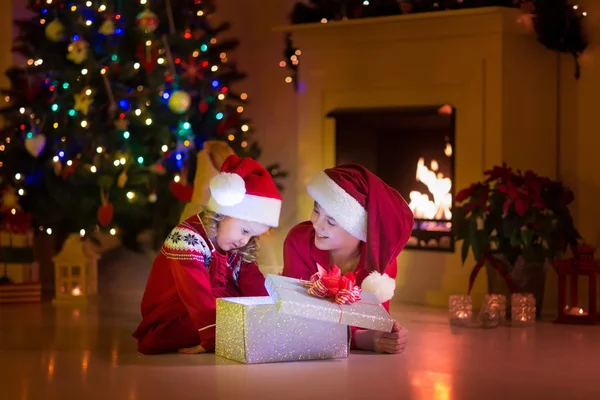 Kinderen openen Kerstcadeaus bij open haard — Stockfoto