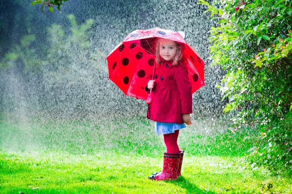 Niña con chaqueta roja jugando bajo la lluvia de otoño — Foto de Stock