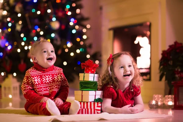 Kinderen openen Kerstcadeaus bij open haard — Stockfoto