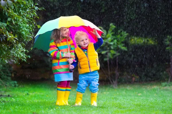 Kinder spielen im Regen unter buntem Regenschirm — Stockfoto