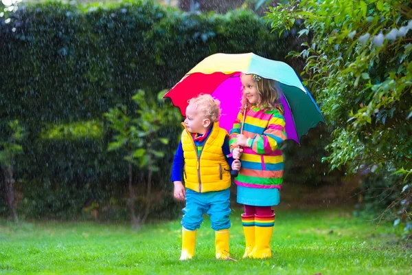 Kinder spielen im Regen unter buntem Regenschirm — Stockfoto