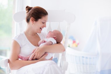 Genç anne ve yenidoğan bebek beyaz yatak odasında