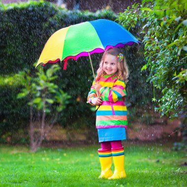 Little girl playing in the rain under colorful umbrella