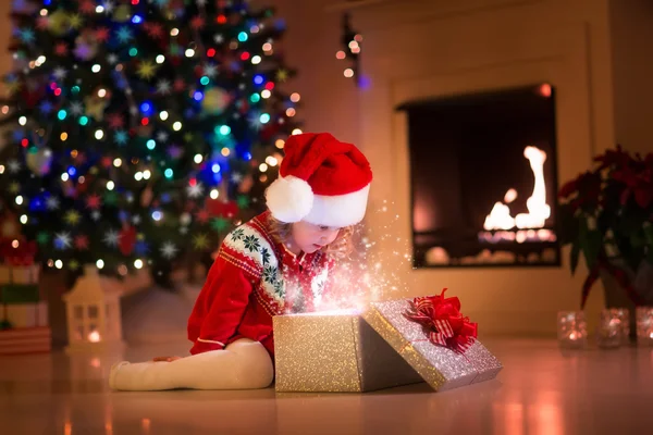 Little girl opening Christmas presents next to a fire place — ストック写真