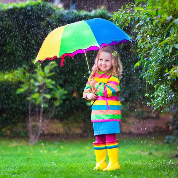 Kleines Mädchen spielt im Regen unter buntem Regenschirm — Stockfoto