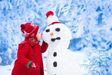 Little girl building snow man in winter