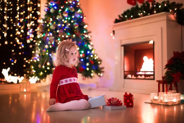 Kleines Mädchen öffnet Weihnachtsgeschenke am Kamin — Stockfoto