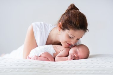 Genç anne ve yenidoğan bebek beyaz yatak odasında