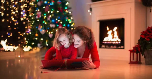 Ibu dan anak membaca buku di perapian pada malam Natal . — Stok Foto