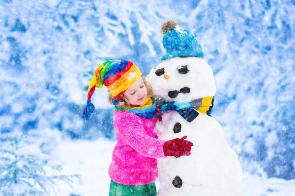 Menina construindo um homem de neve no inverno — Fotografia de Stock