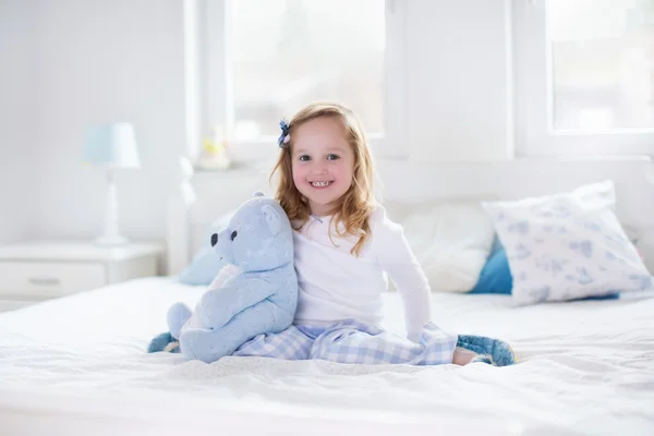 Little girl playing with toy and reading a book in bed — Stock Photo, Image