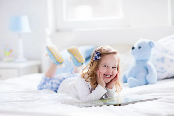 Menina brincando com brinquedo e lendo um livro na cama — Fotografia de Stock