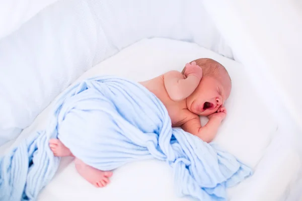 Cute yawning newborn baby in white bed — Stockfoto