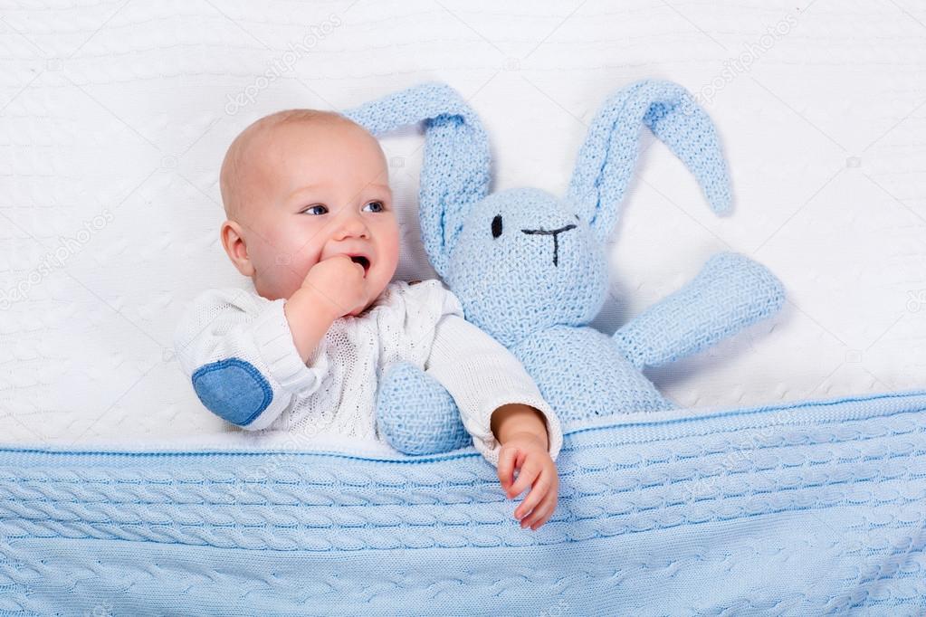 Baby boy playing with blue knitted bunny toy