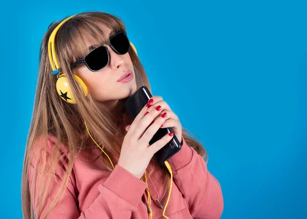 戴耳机和太阳镜的女人 带着智能手机唱歌 蓝色背景 — 图库照片
