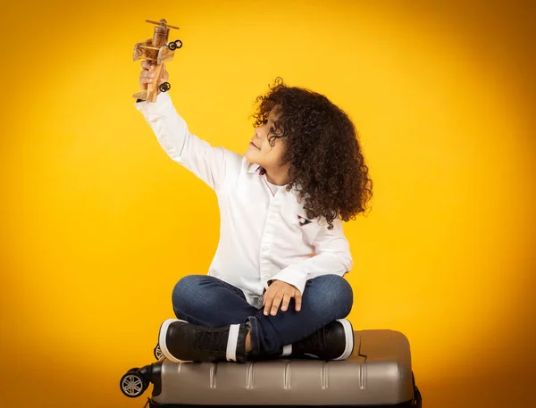 child plays with a plane on top of a suitcase, on yellow background concept travel