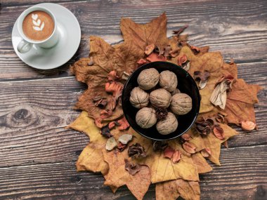 Sonbahar yaprakları ve fındıklı ahşap masada bir kahve.