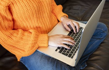 Evdeki kanepede bilgisayar kullanan yüzü olmayan kadın.