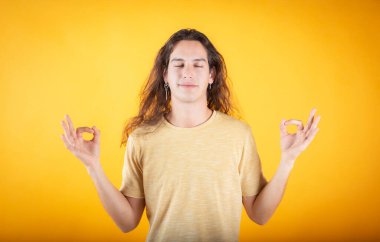 Gündelik kıyafetler giymiş, gözlük takmış, gözleri kapalı gülümseyen, parmaklarıyla meditasyon yapan genç bir İspanyol. yoga konsepti.