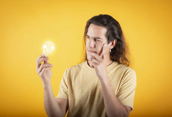 Long haired man dressed in casual t-shirt over isolated yellow background relaxing and smiling with illuminated light bulb, thinking solutions