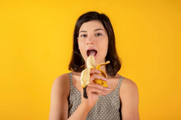 Morena Mujer Ropa Casual Comiendo Plátano Mano Fondo Amarillo Comida —  Fotos de Stock