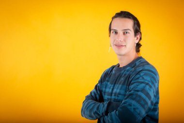 Mavi gözlü ve sıradan elbiseli bir adam kolları çaprazlanmış, sarı arka planda fotokopi alanı olan bir yere bakıyor.