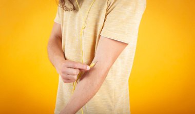 Mavi gözlü ve uzun saçlı bir adam, günlük kıyafetler, sarı şapka kulaklıklı müzik dinleyen bir adam, sarı arka plan.