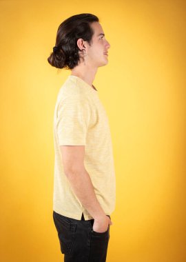 Uzun saçlı, sarı gömlekli, sarı arka planlı, uzun boylu, yakışıklı bir adam.