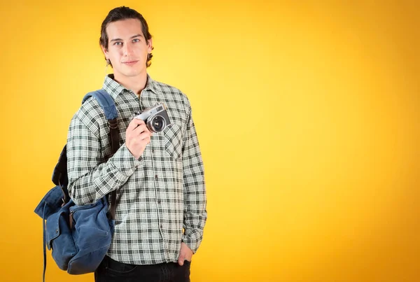 handsome and smiling blue-eyed man, wearing casual clothes,with a backpack and photo camera concept travel, yellow background copy space