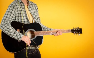 Genç adam gitar öğretmeni, şarkıcı-söz yazarı, gitar çalıyor, sarı arka plan, kopyalama alanı