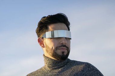 Güneş gözlüklü ve kazaklı bir adam güneşli bir arka plan