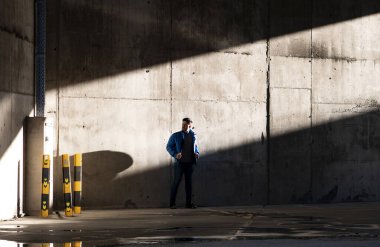 Günlük kıyafetli bir adam, şehir duvarında güneş ışığı ve gölgeler içinde içeri giriyor.,