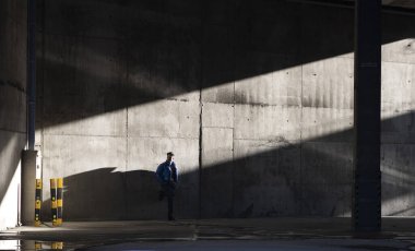 Günlük kıyafetli bir adam, şehir duvarında güneş ışığı ve gölgeler içinde içeri giriyor.,