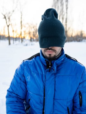 Şapka kaplı, karlı arka planda, gözleri karla kaplı bir adam.