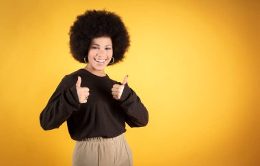 Genç melez Afrikalı Amerikalı kadın izole edilmiş sarı arka planda duruyor. Tamam, parmaklarınla jest yap, mükemmel bir sembol.