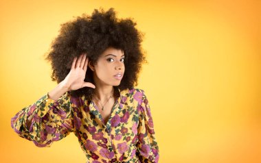 Eli kulağında afro bir kadın, işitme sorunları var, sarı arkaplan