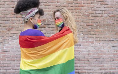 İki farklı ırktan (arkadaşlar veya lgbt çifti) LGBT Onur Günü kutlamalarında gökkuşağı maskeli iki güzel kadın.