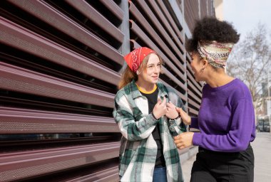 İki çok ırklı kadın sokakta gülüyor ve konuşuyor.