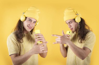 Uzun saçlı bir adam, günlük giysiler, mutlu dans, cep telefonu ve kulaklıkla şarkı söyleyen sarı arka plan, kopyalama alanı