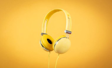 Sarı arka plandaki kulaklıklar havada süzülüyor.