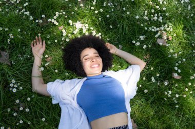 Güzel afro kadın çiçeklerle çimenlerin üzerinde rahatlamış, baharda bir parkta, günlük kıyafetlerle.