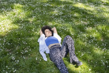 Güzel afro kadın çiçeklerle çimenlerin üzerinde rahatlamış, baharda bir parkta, günlük kıyafetlerle.