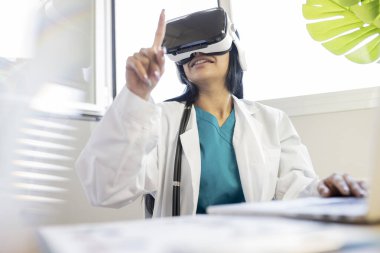 Üniformalı kadın doktor ofisinde, elinde görsel gerçeklik gözlükleriyle oturuyor.