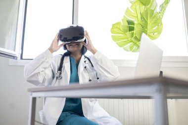 Sanal gerçeklik gözlüğü takan kardiyoloji doktoru ofisinde mutlu oturuyor.